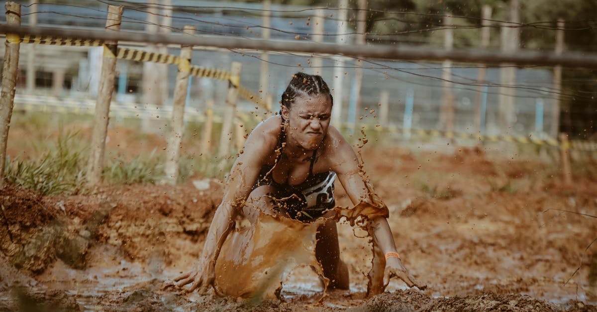 Determined woman crawls through muddy obstacle course in outdoor race challenge.