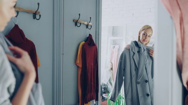Woman trying on a coat in a fitting room, checking in the mirror.