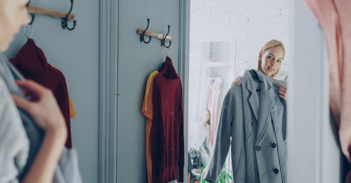 Woman trying on a coat in a fitting room, checking in the mirror.