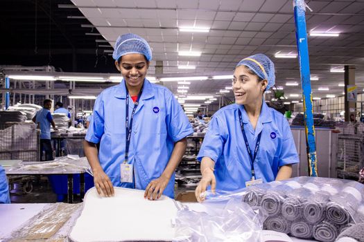 Textile warehouse workers in blue uniforms packing materials with smiles.