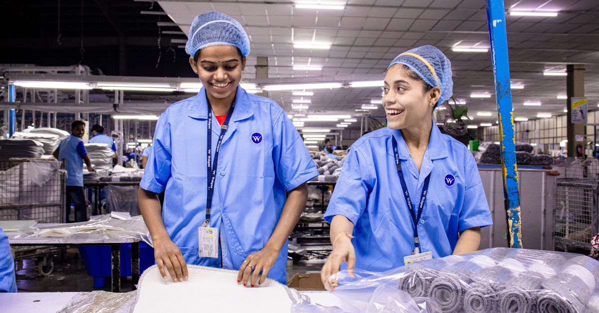 Textile warehouse workers in blue uniforms packing materials with smiles.