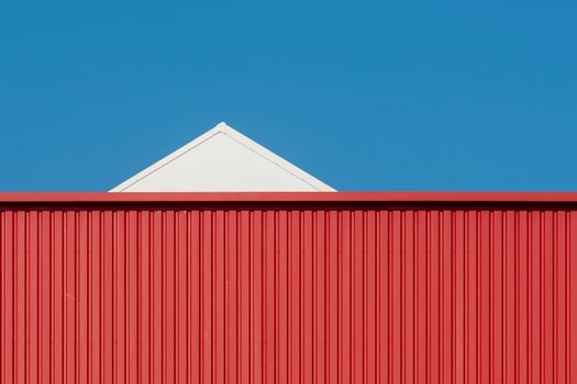 A minimalist photo of a red and white building against a clear blue sky.