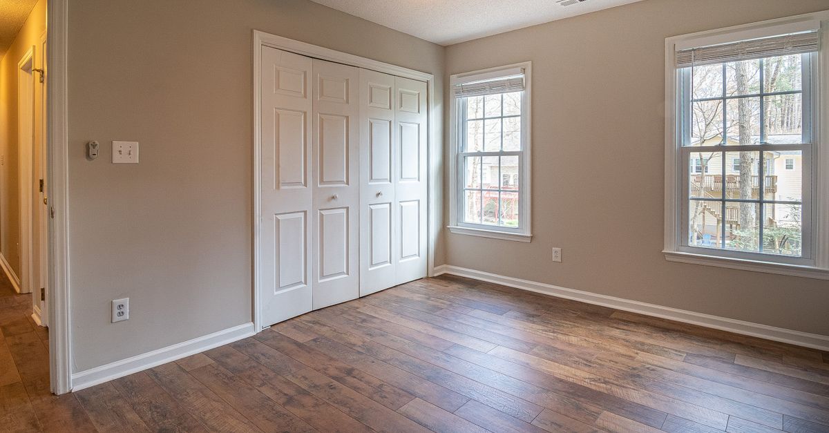 Spacious empty room with hardwood floors, ceiling fan, and natural light from windows.