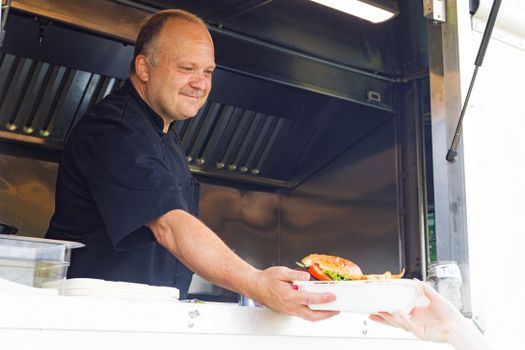 Chef in a food truck handing over a burger plate to a customer with a smile.