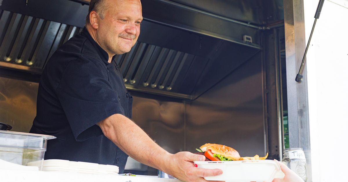 Chef in a food truck handing over a burger plate to a customer with a smile.