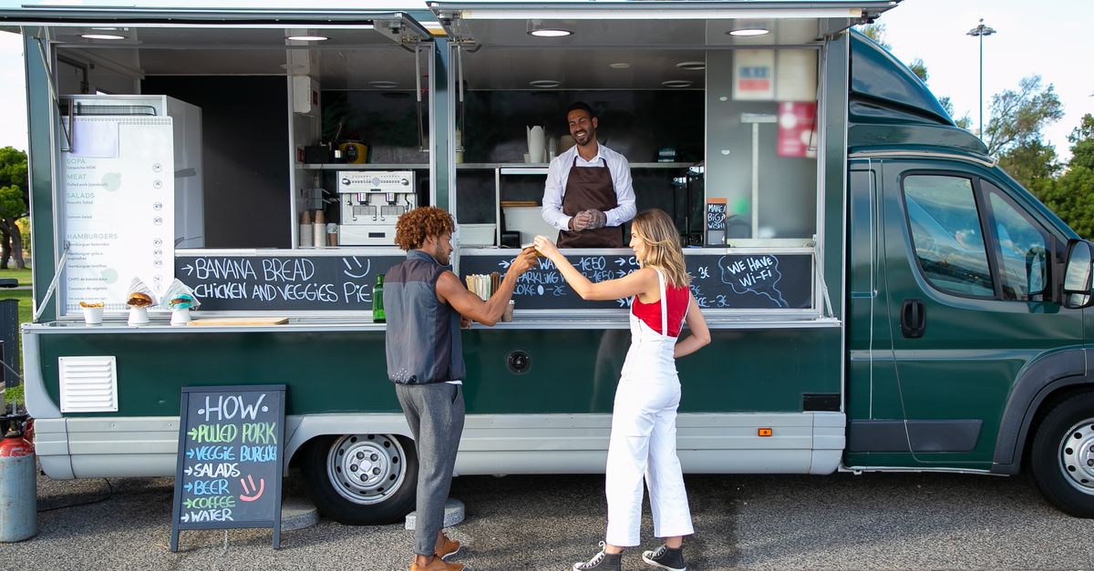 Full body back view full body of multiracial couple toasting with drinks while having lunch at food truck