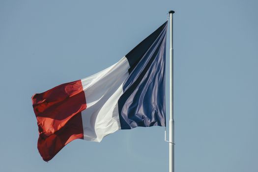Colorful french flag on pole waving in air against blue sky on sunny weather on celebration day in summer outside