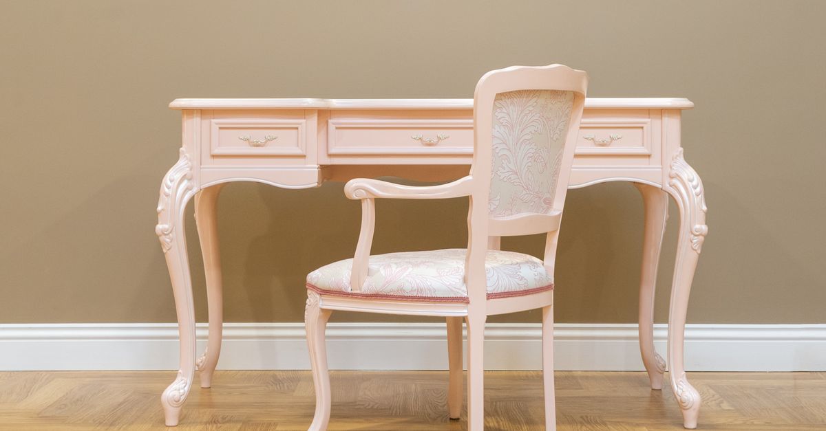 A classic pink vintage desk and matching chair set on a wooden floor with beige wall, perfect for elegant interiors.
