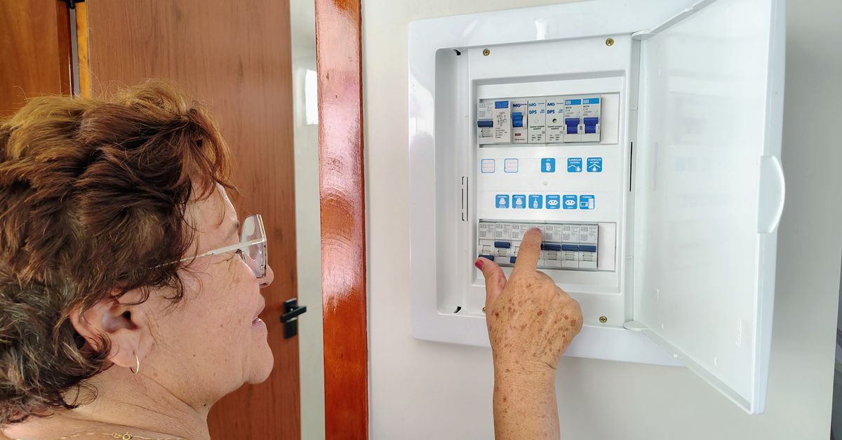 A senior woman is adjusting an electrical fuse panel indoors, demonstrating home safety.