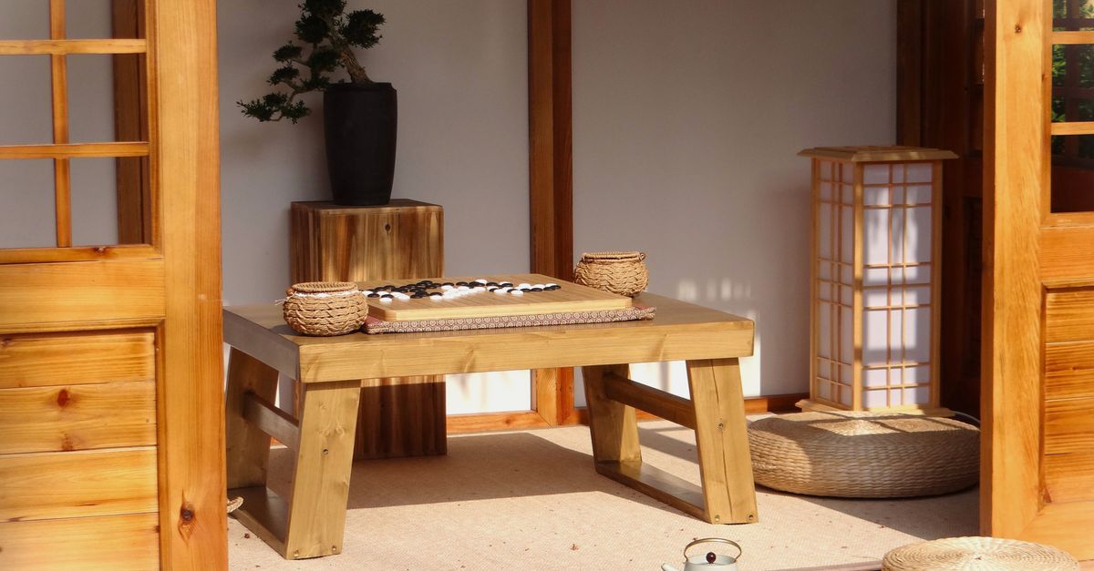 Tranquil Japanese Zen room featuring a Go board, tea set, bonsai tree, and wicker cushions on a wooden table.