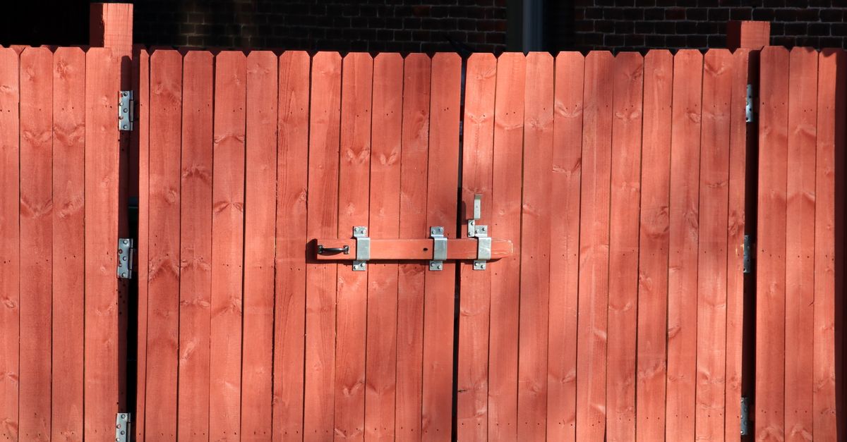 Rustic red wooden fence with a metal latch, ensuring safety and security outdoors.