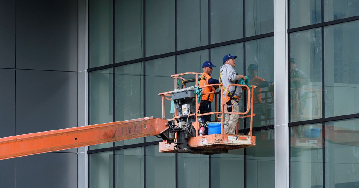 Two workers clean large glass windows using a cherry picker lift outside a building in Canonsburg, PA.