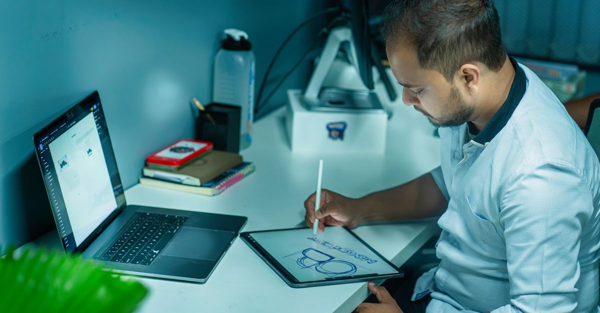 A focused man uses a tablet to design while working at his desk in a modern office setting.