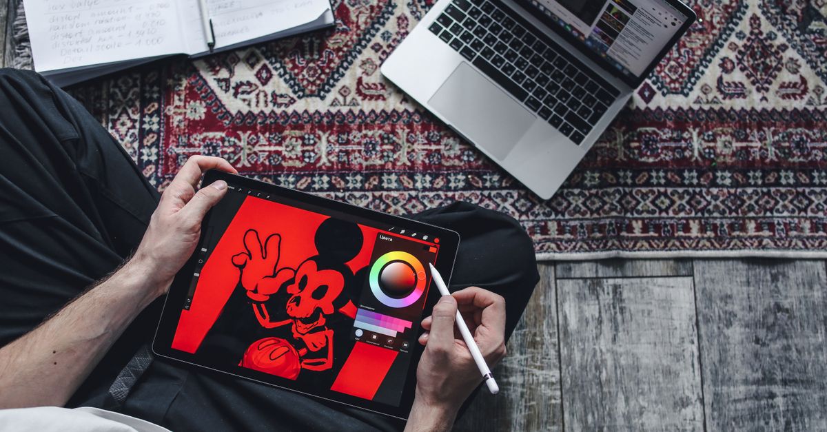 A person drawing on a digital tablet while seated on a patterned rug indoors.