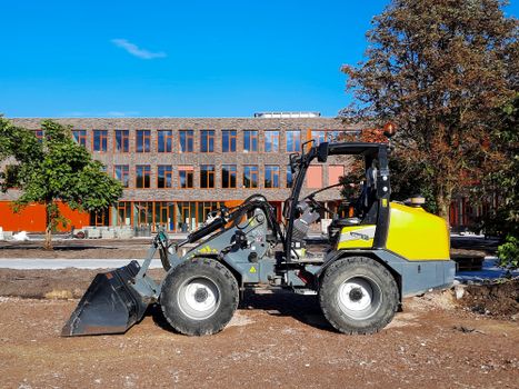 Yellow loader machine at a construction site with modern building background.