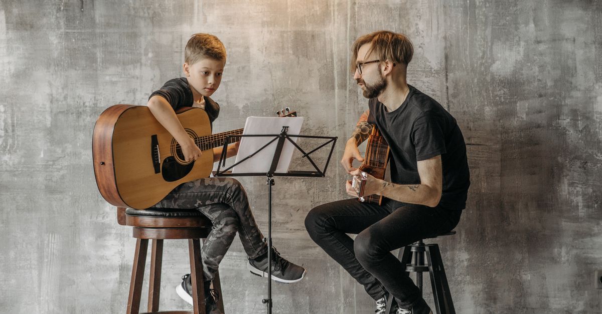 A child learning to play the guitar under the guidance of a teacher in a cozy indoor setting.