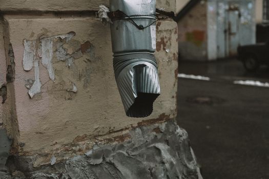 A metal drainage pipe with a rustic appearance on an aged wall with flaking paint.