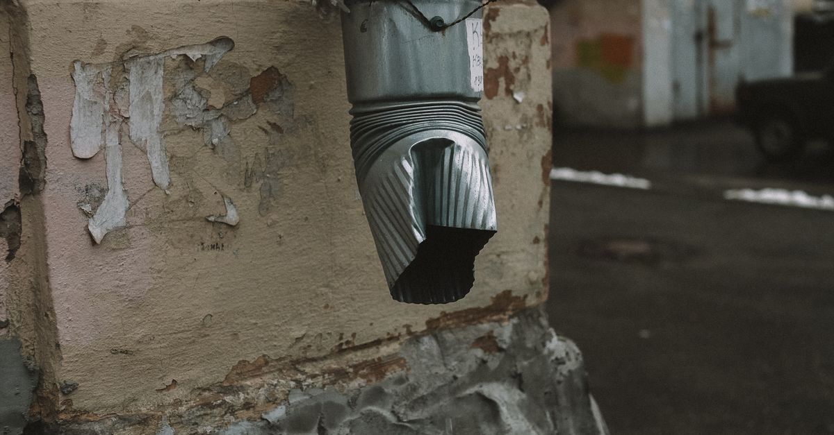 A metal drainage pipe with a rustic appearance on an aged wall with flaking paint.
