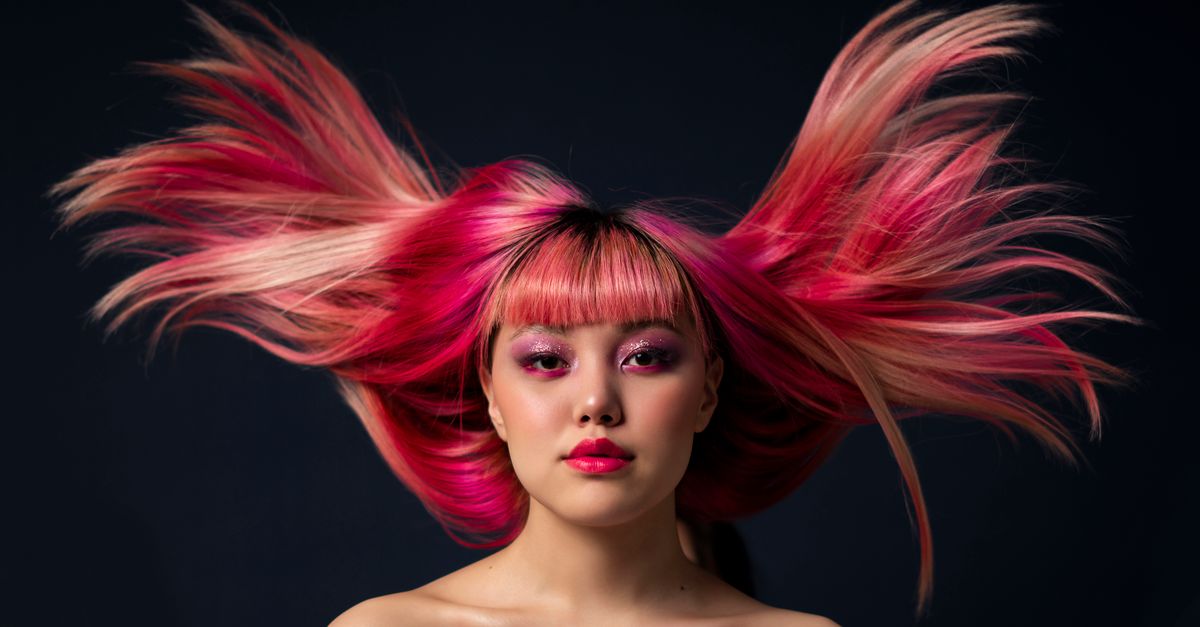 Captivating portrait of woman with vibrant pink hair against a dark background.