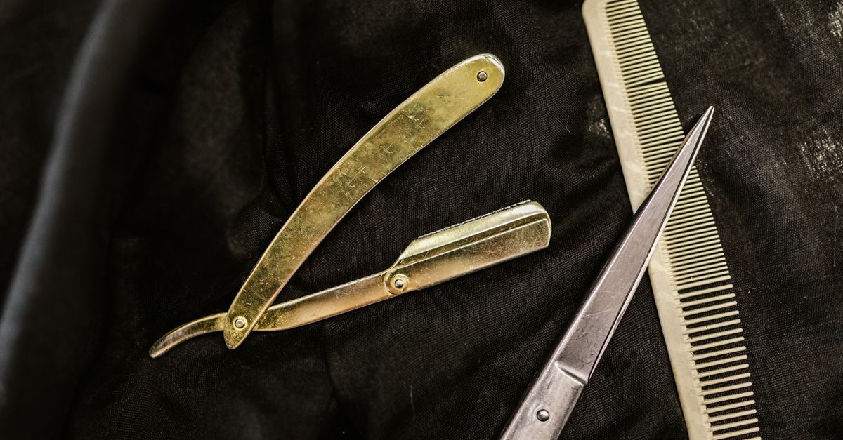 Close-up of silver shears, comb, and straight razor on a black cloth background, highlighting barber tools.