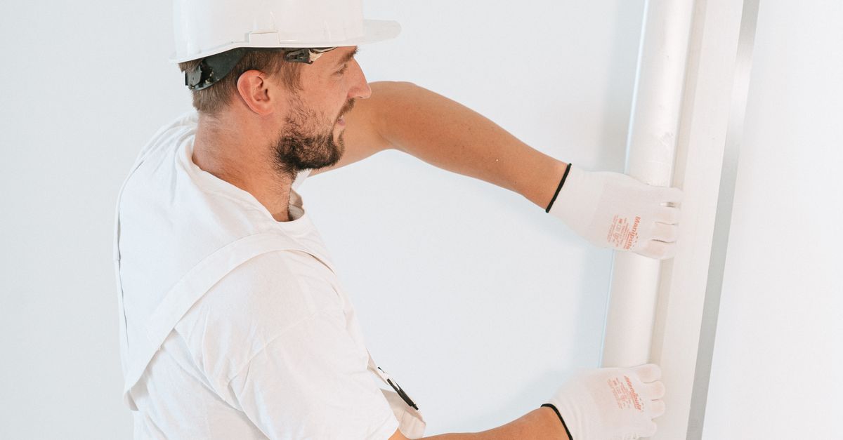 Professional construction worker installing drywall with gloves and helmet inside a building.