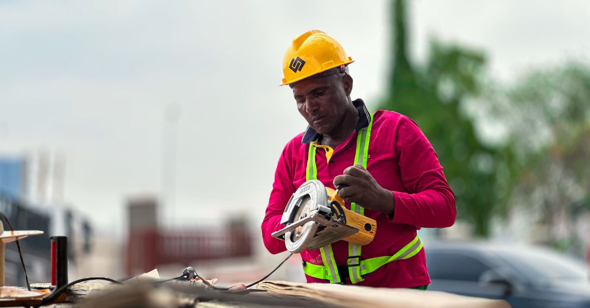 A construction worker in a hard hat operates a circular saw on a building site.