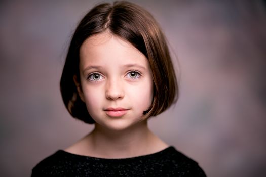 Portrait of cute young girl with blight green eyes and perfect hairstyle looking at camera against blurred background