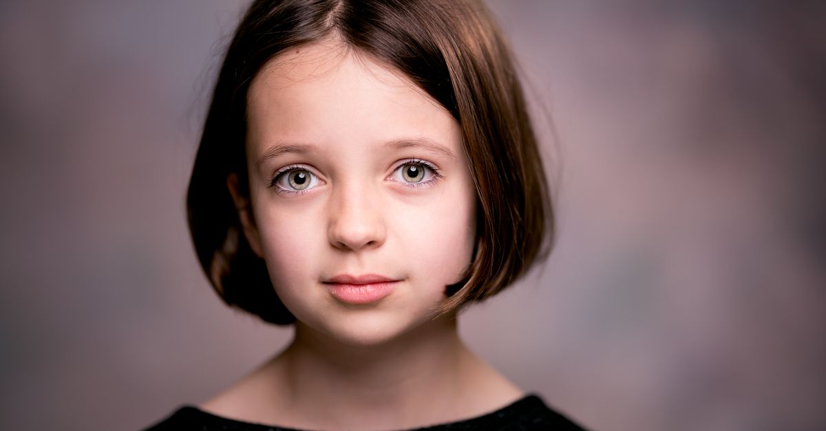 Portrait of cute young girl with blight green eyes and perfect hairstyle looking at camera against blurred background
