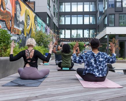 A diverse group of adults practicing yoga outdoors in a vibrant urban setting.