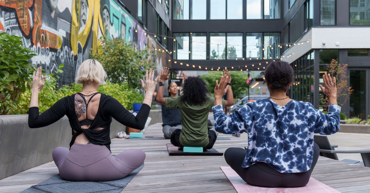 A diverse group of adults practicing yoga outdoors in a vibrant urban setting.