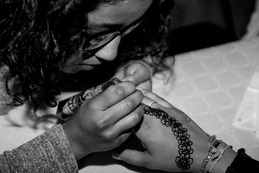 Close-up of woman applying intricate henna tattoo design on hand.