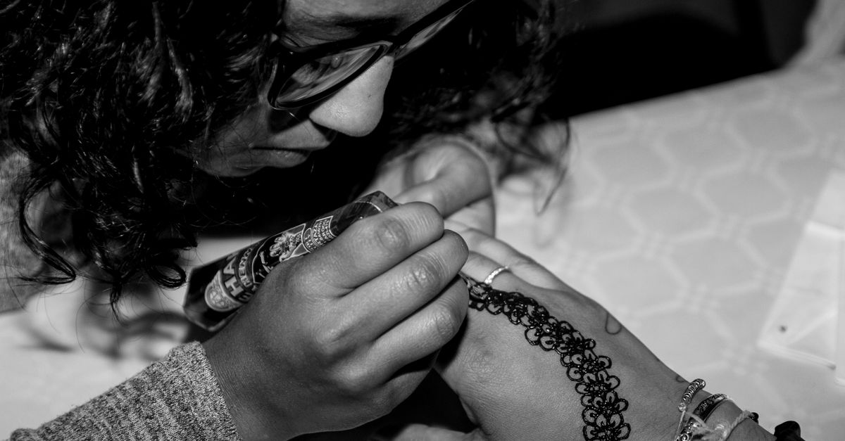 Close-up of woman applying intricate henna tattoo design on hand.