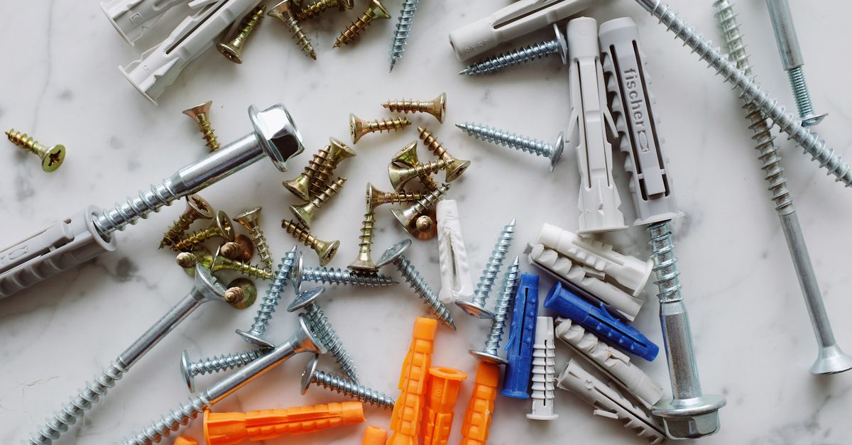 Set of assorted multicolored plastic dowels and various metal screws of different sizes placed on white marble table in workshop