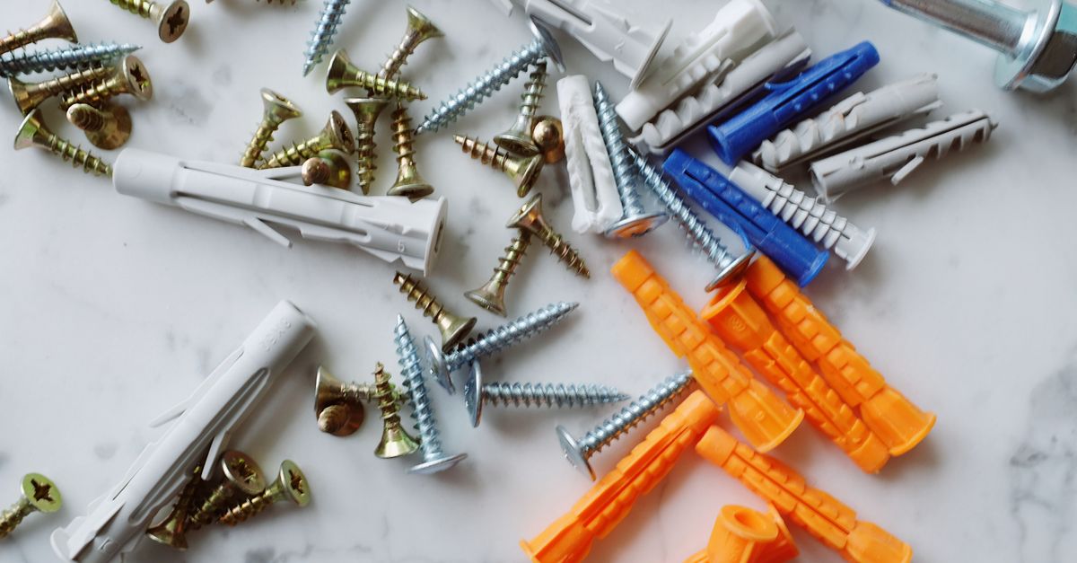 Set of various multicolored plastic dowels with assorted metal screws of different sizes placed on white marble table in modern workshop