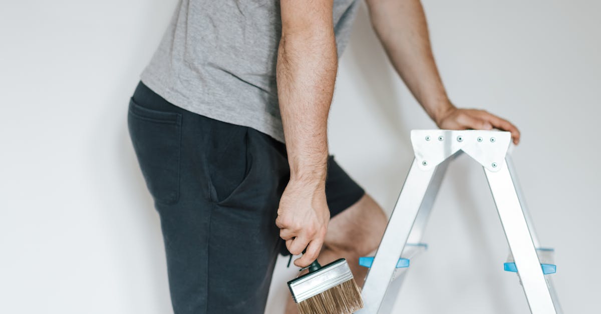 Side view of crop anonymous male decorator in casual clothes preparing to painting walls of light room while standing on stepladder