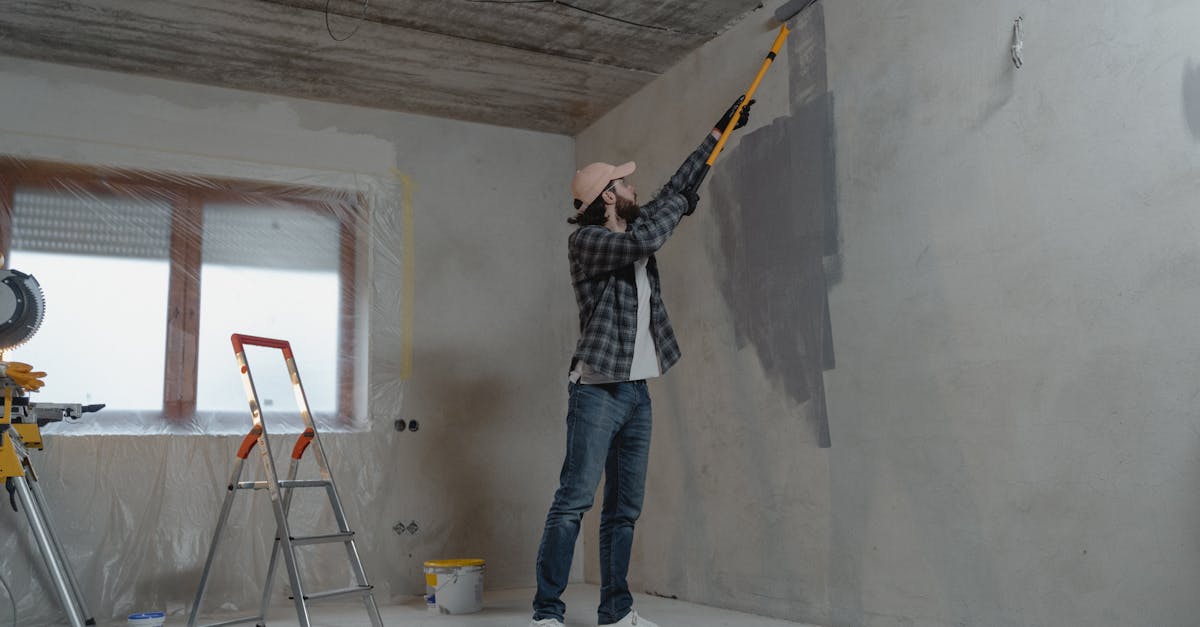 A man painting an interior wall with a roller during a home renovation project.