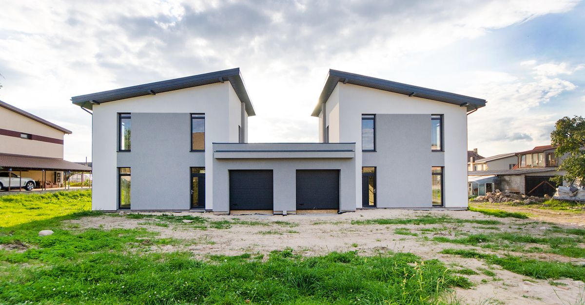 Front view of twin modern houses with a symmetrical architectural design under a cloudy sky.