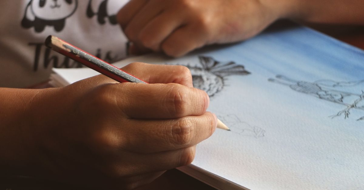 Hand sketching in a notebook with pencil, displaying artistic creativity.