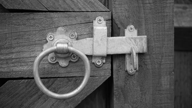 Close-up of a rustic wooden gate featuring a metal latch with a ring handle, blending vintage and security elements.