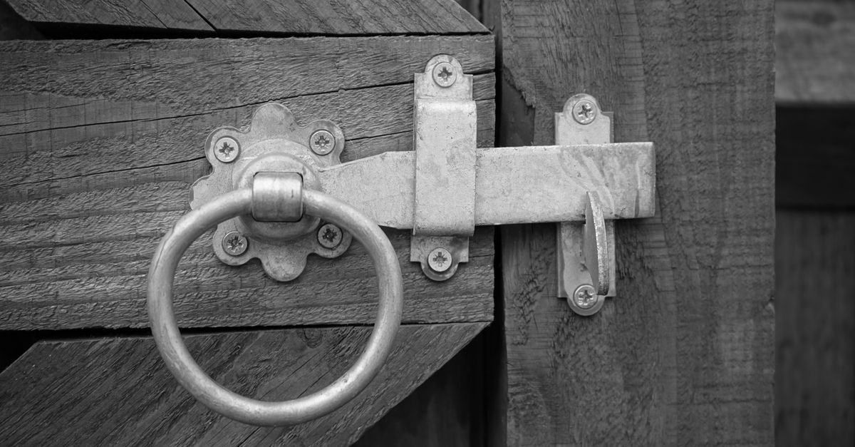 Close-up of a rustic wooden gate featuring a metal latch with a ring handle, blending vintage and security elements.