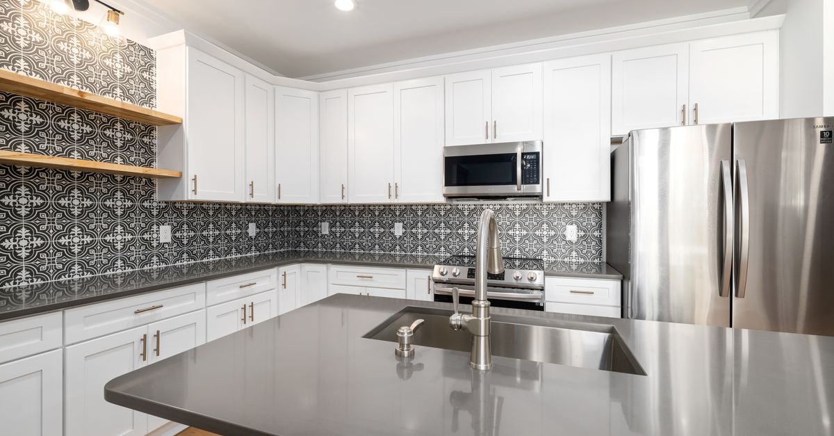 Stylish white kitchen featuring a geometric tile backsplash and stainless steel appliances.