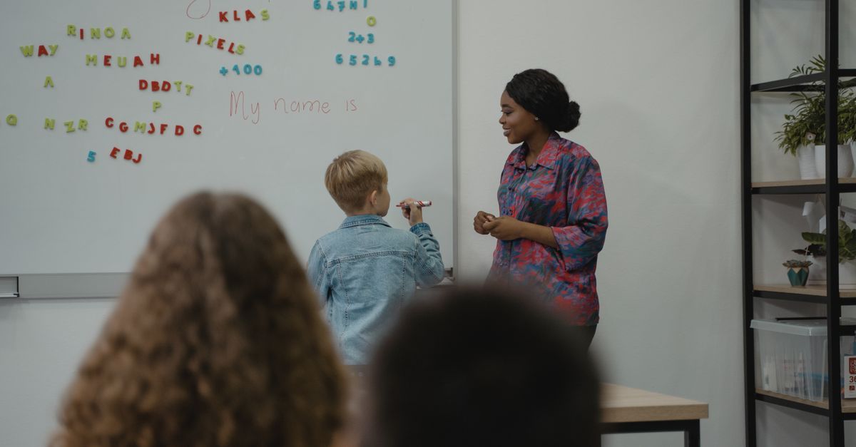 A teacher engages students in an interactive English lesson using a whiteboard and magnetic letters.