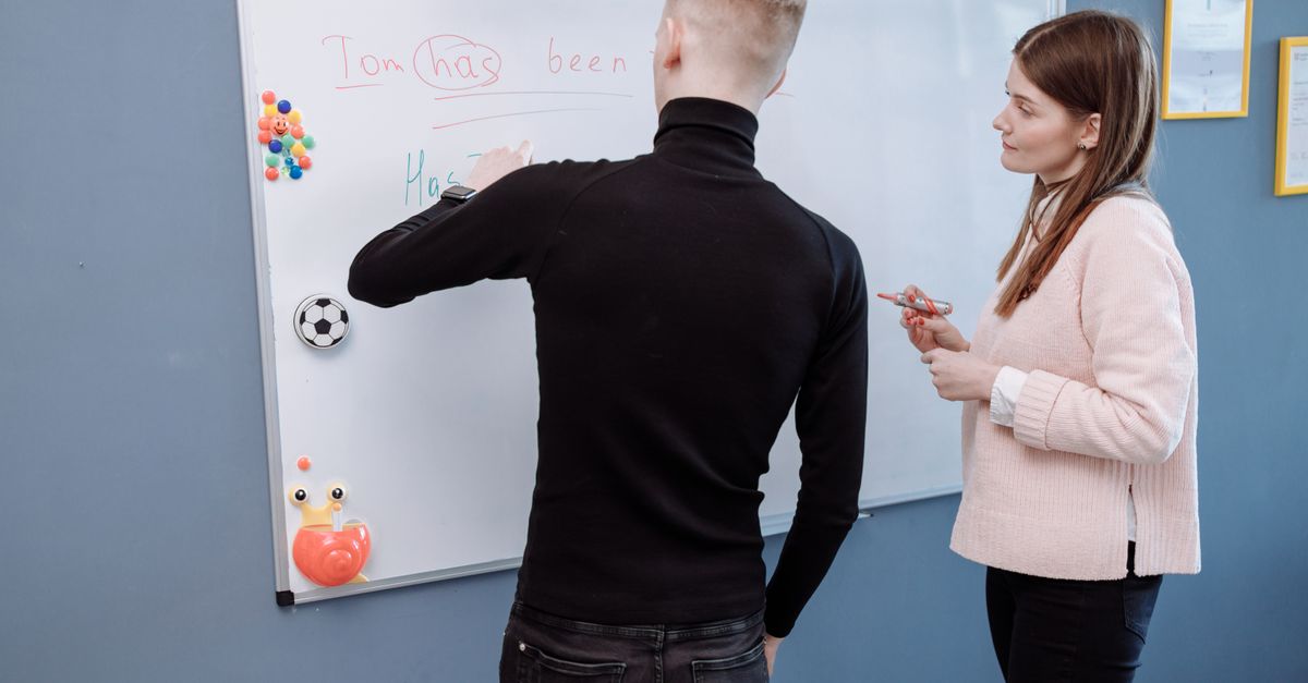 A student and teacher engage in an English lesson on a whiteboard. Indoor educational setting.