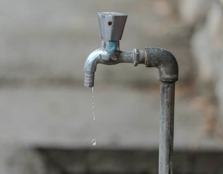 Close-up image of an outdoor water tap with a single droplet falling, highlighting water conservation.