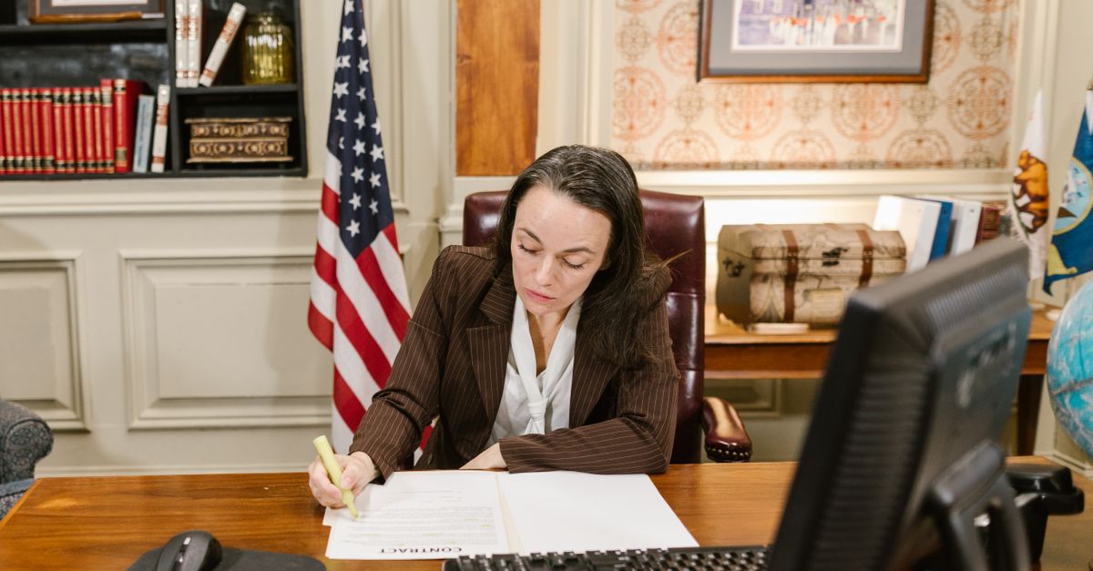 Female attorney in a law office signing legal documents at her desk, surrounded by legal books and symbols of justice.