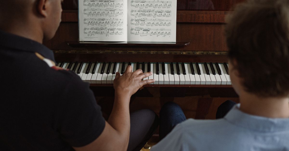 A close-up view of a teacher and a student playing piano during a lesson.