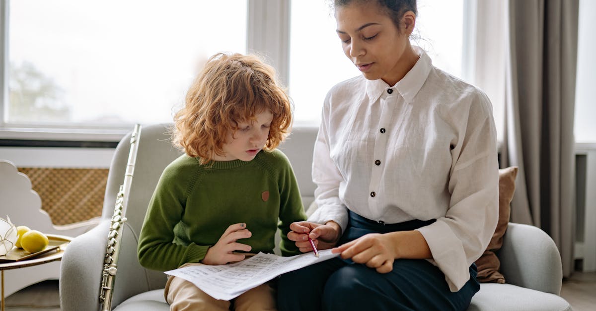 A young boy is learning music indoors with his teacher, playing the flute and reading sheet music.