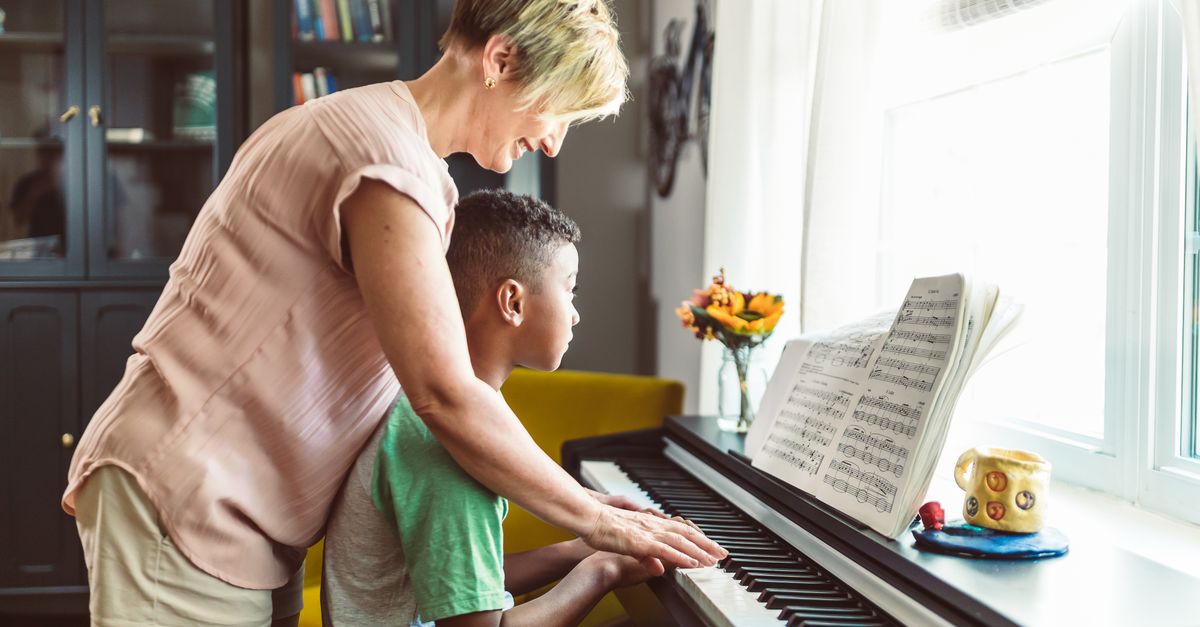 A woman teaches a young boy how to play the piano, focusing on sheet music.