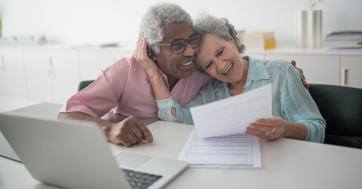 A joyful senior couple smiling while reviewing documents together at a desk with a laptop.