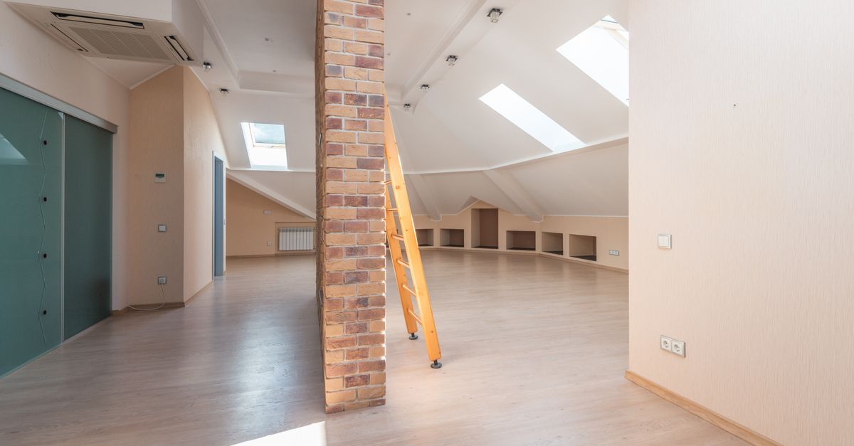 Spacious attic room with natural light from skylights, featuring a brick pillar and a wooden ladder.